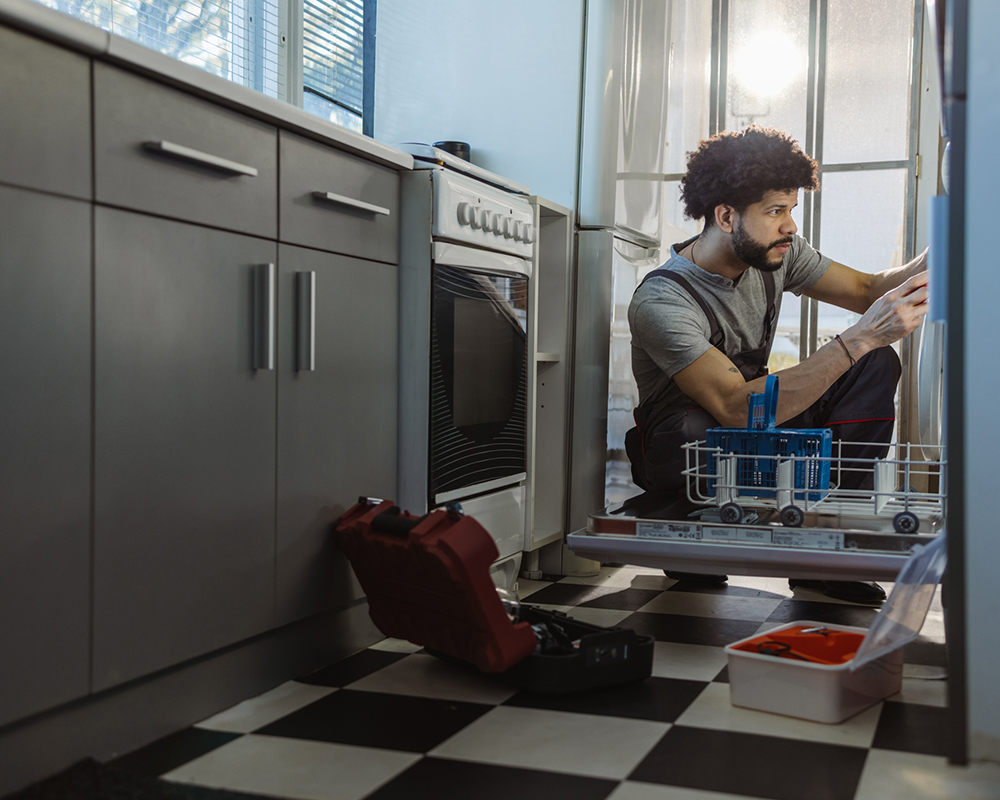 Young Latin handyman repairs the dishwasher in the client's kitchen